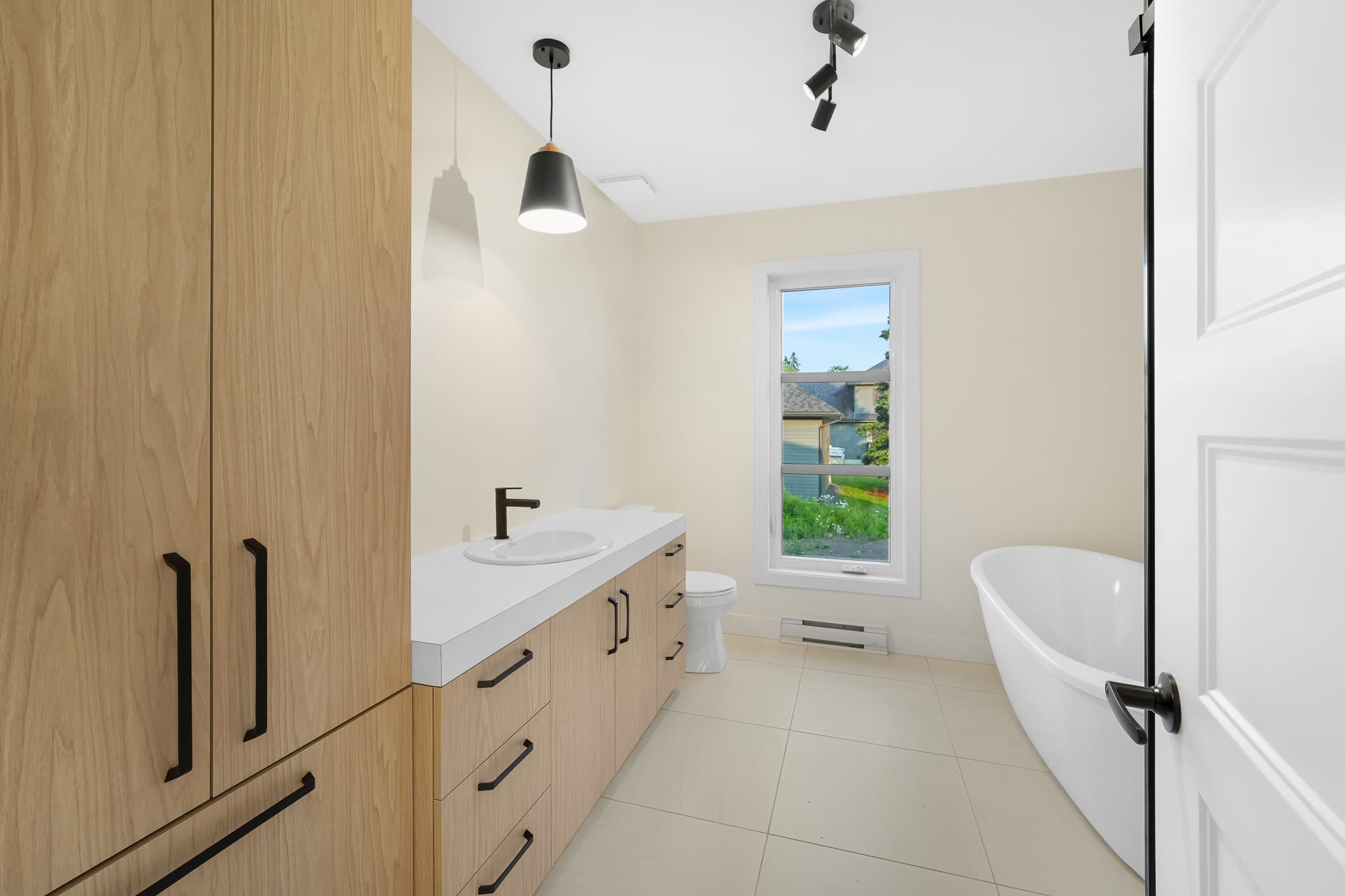 Salle de bain lumineuse du modèle La Bellevue, avec baignoire autoportante, bois clair et robinetterie noire.